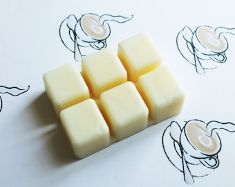 May include: Six white wax melts arranged in a grid pattern on a white surface. The wax melts are square shaped and have rounded edges.