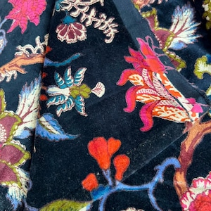 Peut inclure: Un tissu en velours noir orné d'un motif floral vibrant avec des détails brodés dans des tons de rose vif, orange, bleu, vert et blanc. Le textile présente un design botanique dense avec des fleurs, des feuilles et des branches stylisées.