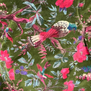 May include: Close-up of a green fabric with a vibrant floral and bird pattern. The design features pink flowers, birds with red and blue accents, and various leaves. The fabric has a soft, velvety texture, creating a rich and detailed aesthetic.