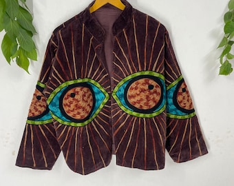 Könnte beinhalten: Braune Samtjacke mit offenem Schnitt. Die Jacke hat große Augendesigns auf der Vorderseite und den Ärmeln mit türkisfarbenen, grünen und orangefarbenen Akzenten. Das Design umfasst strahlenförmige Linien in Braun- und Goldtönen.