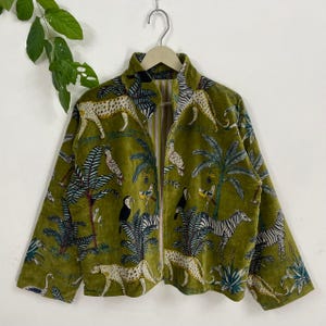 Könnte beinhalten: Olivgrüne Samtjacke mit durchgehendem Reißverschluss. Die Jacke hat ein Dschungel-Thema mit Geparden, Zebras, Vögeln und Palmen. Die Jacke hat einen hohen Kragen und lange Ärmel.