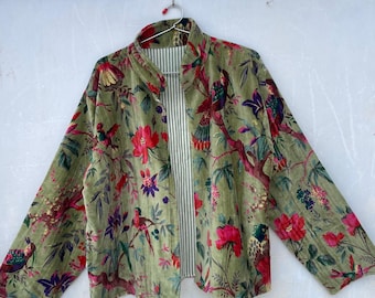 Op de afbeelding: Groene fluwelen jas met een bloemen- en vogelpatroon. De jas heeft een opstaande kraag en lange mouwen. De binnenvoering is gestreept in wit en groen. De jas hangt aan een hanger met een gele smiley.