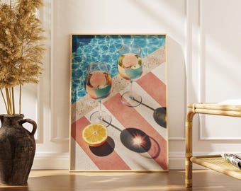 Könnte beinhalten: Gerahmter Kunstdruck mit zwei Weingläsern, gefüllt mit bunten Getränken, einer halben Orange und einer Poolszene. Das Kunstwerk hat einen goldenen Rahmen und steht vor einer weißen Wand mit einer Vase mit getrockneten Pflanzen.