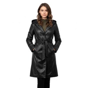 Può includere: Un cappotto in pelle nera con cappuccio e cintura. Il cappotto ha una chiusura con bottoni e tasche. La modella indossa un dolcevita verde. Il cappotto è lungo fino al ginocchio e ha un design classico.