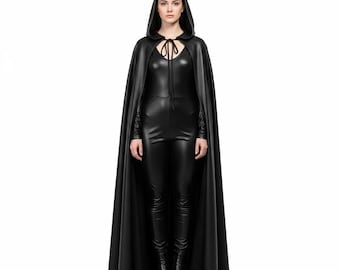 May include: A full-length image of a person wearing a black hooded cape with a tie closure at the neck. The cape is paired with a black jumpsuit and boots. The outfit has a sleek, gothic aesthetic.
