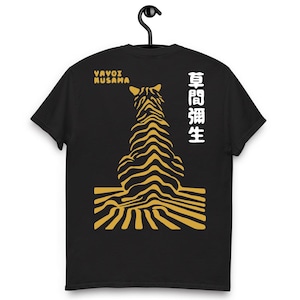 Puede incluir: Camiseta negra con un diseño de tigre estilizado en amarillo y negro. La parte trasera de la camiseta muestra el texto "YAYOI KUSAMA" en amarillo y caracteres japoneses en blanco.