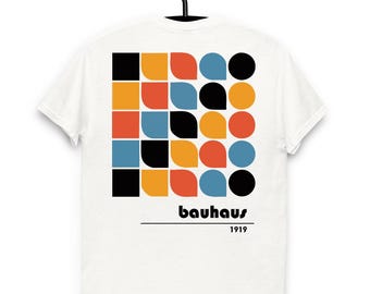May include: White t-shirt with a colorful geometric design on the back, featuring squares, circles, and curved shapes in black, orange, red, and blue. The word "bauhaus" and the year "1919" are printed below the design.