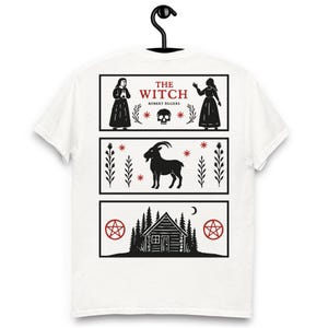 Puede incluir: Camiseta blanca con un diseño gráfico negro. El diseño muestra tres paneles: arriba, "THE WITCH" y "ROBERT EGGERS", en el medio una cabra y abajo una cabaña en el bosque con luna y pentagramas.