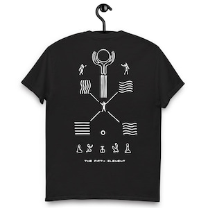 Puede incluir: Camiseta negra con un diseño gráfico blanco que presenta figuras y símbolos abstractos. El texto "THE FIFTH ELEMENT" está impreso en la parte inferior. La camiseta está colgada en una percha negra.