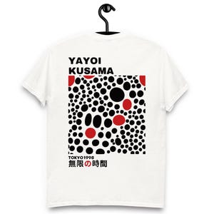 Può includere: T-shirt bianca con un motivo a pois neri e rossi e la scritta "YAYOI KUSAMA" sopra il disegno. Sotto il disegno c'è la scritta "TOKYO 1998" e testo giapponese. La maglietta è appesa a una gruccia nera.