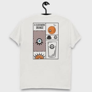 Peut inclure: T-shirt blanc avec un motif graphique inspiré de "Orange Mécanique". Le motif comprend une orange avec un œil, un chapeau melon, un verre de liquide et le texte "A Clockwork Orange".