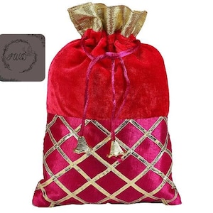 May include: A red velvet drawstring bag with a gold and pink diamond pattern on the bottom. The top of the bag is a gathered gold fabric. The bag has a drawstring closure with pink cords and gold bell charms.