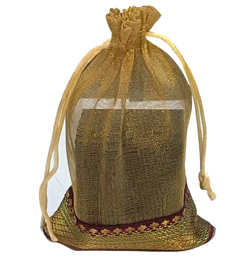 May include: A gold-colored, sheer drawstring bag. The bag is filled with an unseen object. The bottom of the bag has a decorative band with a red and gold pattern. The drawstring is a light beige color.