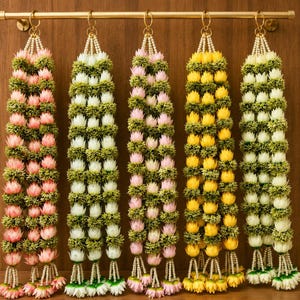 May include: Five vertical floral garlands hanging from a gold metal rod. Each garland features alternating rows of small green textured foliage and rounded flower buds in shades of light pink, white, and yellow, finished with white bead accents.