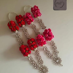 以下が含まれることがあります： 赤とピンクのバラと銀色の装飾が施された、いくつかの花のガーランド。各ガーランドは上部にループ、下部に装飾的なペンダントが付いています。ガーランドは明るい色の表面に配置されています。
