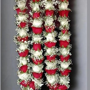 May include: Three strands of flower garlands, each composed of alternating red and white roses, interspersed with small white flowers. The garlands are suspended from a beaded string, creating a vertical display.