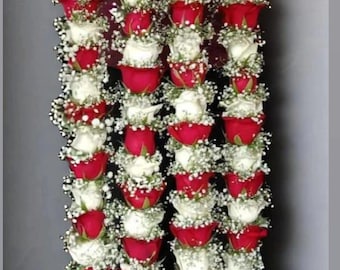 May include: Three strands of flower garlands, each composed of alternating red and white roses, interspersed with small white flowers. The garlands are suspended from a beaded string, creating a vertical display.