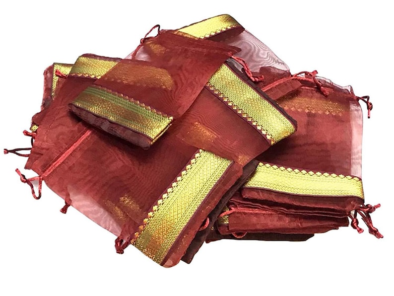 May include: A collection of maroon organza drawstring bags with gold trim. The bags are piled together, showcasing their sheer texture and decorative gold borders. The drawstring closures are a matching maroon color.