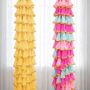 Op de afbeelding: Twee decoratieve hangornamenten. Eén is geel met gouden rand, de andere is roze, lichtblauw en roze met gouden rand. De ornamenten zijn gemaakt van gelaagde stof en hangen aan een goudkleurige haak.