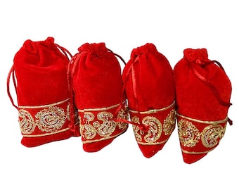 May include: Four red velvet drawstring bags with gold embroidered trim. The bags are closed with matching red drawstrings. The gold trim features an ornate paisley design. The bags are arranged in a row.