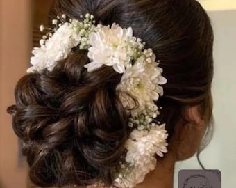 May include: A dark brown updo hairstyle adorned with white flowers and baby's breath. The hair is styled in a bun with loose curls, and the flowers are arranged around the bun. The image is taken from the back, showing the hairstyle and part of the neck.