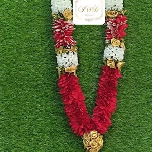 Pode incluir: Uma grinalda decorativa com elementos florais brancos, vermelhos e dourados. A grinalda tem um pendente central com rosas vermelhas e um adorno dourado. O texto "IWD" é visível em um rótulo branco.