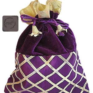 May include: A purple velvet drawstring bag with a gold satin top and gold accents. The lower portion features a purple fabric with a gold diamond pattern. The bag has gold tassels and a small logo on the side.