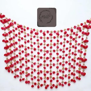 May include: A decorative red pom-pom garland with gold-colored connecting chains. The garland is arranged in a curved shape. A gray square with the text "FWD" in a circular design is in the upper right corner.