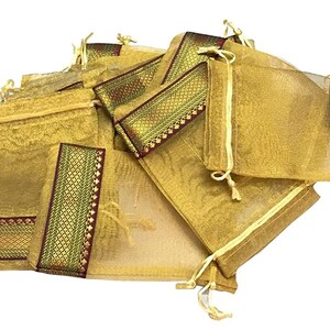 May include: A collection of gold-colored, sheer drawstring pouches. Each pouch has a decorative band of gold, green, and burgundy fabric. The pouches are gathered together, creating a visually appealing display.