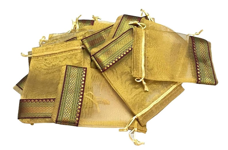 May include: A collection of gold-colored, sheer drawstring pouches. Each pouch has a decorative band of gold, green, and burgundy fabric. The pouches are gathered together, creating a visually appealing display.