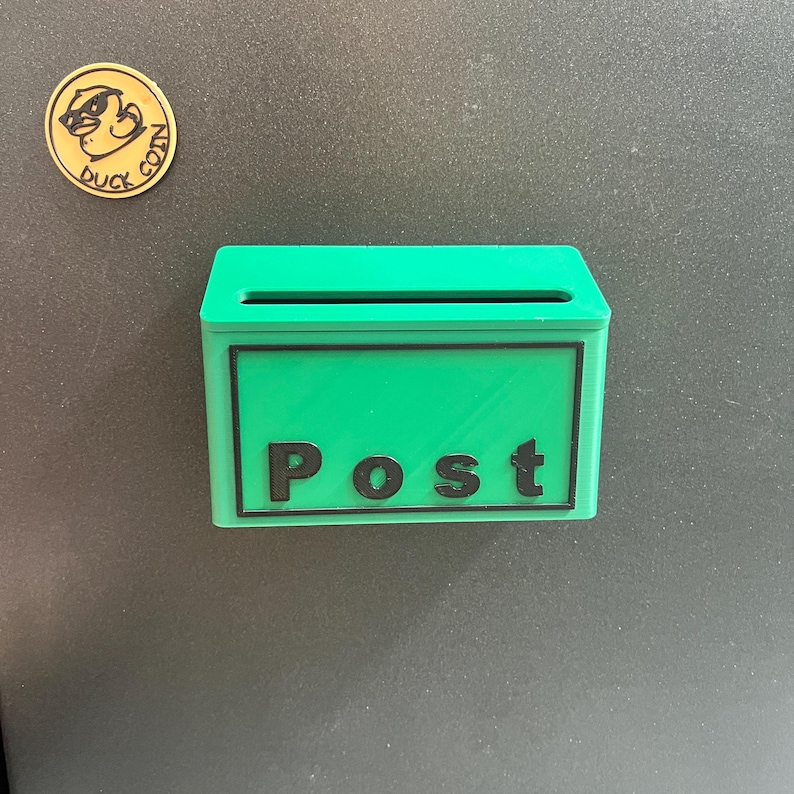 May include: A bright green rectangular wall-mounted mailbox with a horizontal slot and the word Post in black lettering on the front. Above the mailbox is a circular gold-colored coin with a duck illustration and the text Duck Coin.