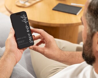 May include: A person holding a black smartphone displaying a wedding invitation. The screen features the words "save our date" in white script, along with the names "Kristen & Paul" and event details. The phone is held against a blurred background.