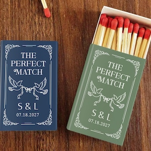 May include: Two matchboxes, one blue and one green, with the text "THE PERFECT MATCH" and a dove design. The blue box is closed, while the green box is open, revealing red-tipped matches. The boxes also display initials and a date.