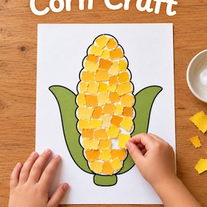 May include: A white sheet of paper with the text Corn Craft at the top, featuring a printed outline of a corn cob filled with small, torn pieces of yellow and orange paper, flanked by green husks, with loose yellow paper scraps nearby.