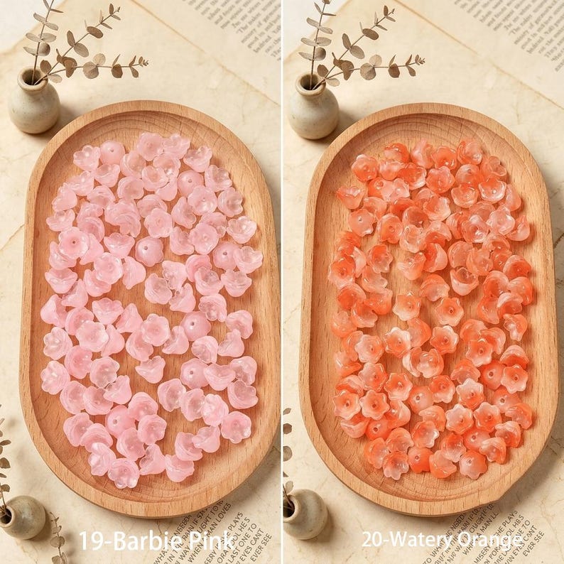 May include: Two oval wooden trays containing small flower-shaped beads. The left tray holds light pink beads labeled 19-Barbie Pink, while the right tray holds orange beads labeled 20-Watery Orange. Each tray is accompanied by a small vase.