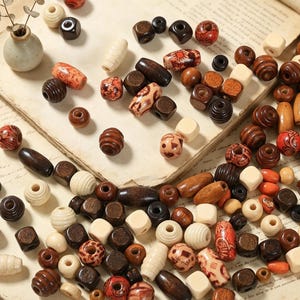 May include: A collection of assorted wooden beads in various shapes, sizes, and finishes, including natural light wood, dark brown, and reddish-orange tones, some featuring intricate patterns and carved textures, scattered across a flat surface.