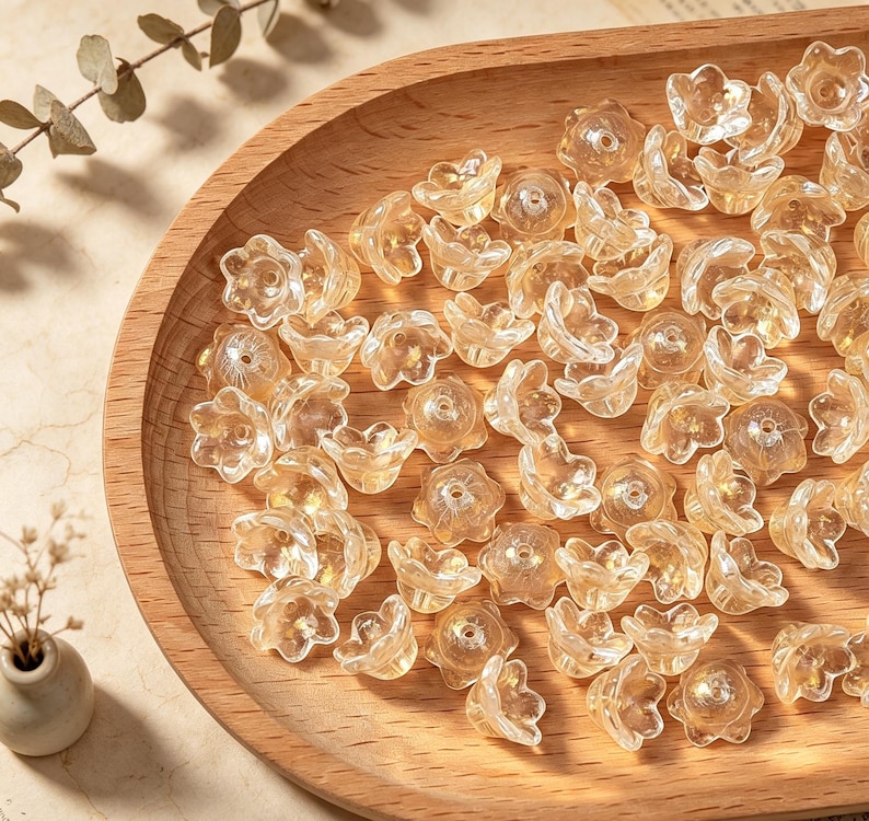 May include: A collection of small, translucent, light amber-colored flower-shaped beads. Each bead features a five-petaled design with a central hole for threading, crafted from a clear material that catches the light to create a subtle glow.