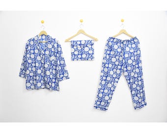 May include: A blue and white floral print pajama set, including a button-down shirt, pants, and a matching eye mask. The set is displayed on wooden hangers against a white background. The floral pattern is a repeating design.