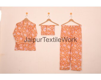 May include: An orange pajama set with a floral pattern, including a button-down shirt, a matching top, and pants. The set is hanging on wooden hangers against a light background. The text "Jaipur Textile Work" is visible.