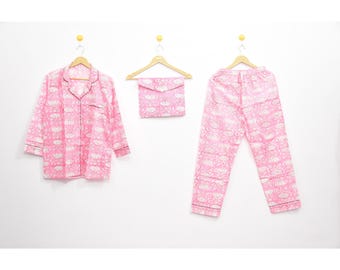 May include: A pink pajama set with a white floral pattern, including a button-down shirt, pants, and a matching pouch. The set has black trim and is displayed on wooden hangers against a white background.