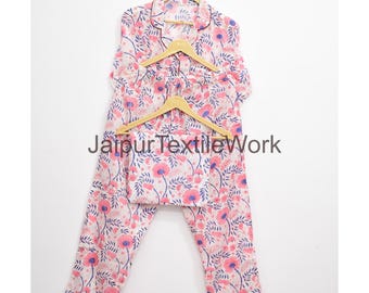 May include: A two-piece pajama set with a floral pattern in pink, blue, and white. The set includes a button-down top and pants, both hanging on wooden hangers. The text "Jaipur Textile Work" is visible.