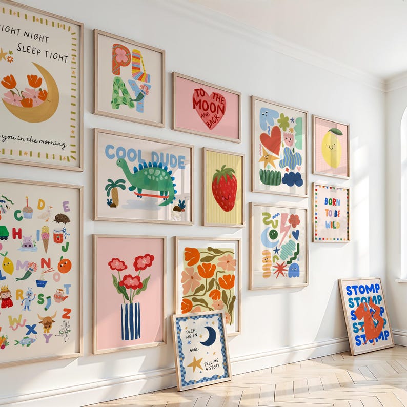 Puede incluir: Una colecci&oacute;n de l&aacute;minas art&iacute;sticas enmarcadas con diversas ilustraciones y texto. Las l&aacute;minas presentan dise&ntilde;os coloridos, incluyendo un dinosaurio, una fresa, flores y frases como "Cool Dude" y "To the Moon and Back". Los marcos son de madera clara.
