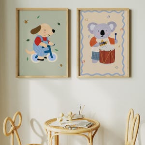 K&ouml;nnte beinhalten: Zwei gerahmte Kinderkunstdrucke. Einer zeigt einen Cartoon-Hund auf einem blauen Fahrrad, der andere einen Koala, der Schlagzeug spielt. Die Drucke haben Holzrahmen und werden an einer wei&szlig;en Wand ausgestellt.