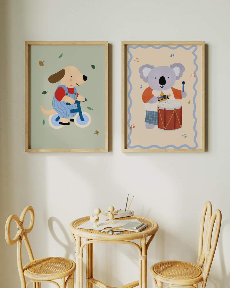 K&ouml;nnte beinhalten: Zwei gerahmte Kinderkunstdrucke. Einer zeigt einen Cartoon-Hund auf einem blauen Fahrrad, der andere einen Koala, der Schlagzeug spielt. Die Drucke haben Holzrahmen und werden an einer wei&szlig;en Wand ausgestellt.
