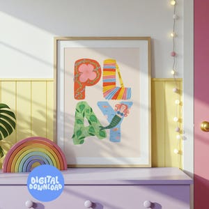 Könnte beinhalten: Ein gerahmter Kunstdruck mit dem Wort "PLAY" in farbenfrohen, skurrilen Buchstaben. Das "P" ist mit einer Blume verziert, das "L" mit Regenbogenstreifen, das "A" mit Blättern und das "Y" mit einer Meerjungfrau. Ein Holzregenbogen und ein "DIGITAL DOWNLOAD"-Aufkleber sind im Vordergrund.