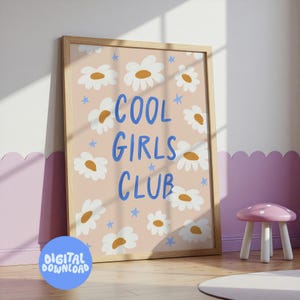 以下が含まれることがあります： 明るい茶色の木製フレームに入ったプリント。プリントは、白いデイジーと青い星が描かれた薄いピンク色の背景です。「COOL GIRLS CLUB」という言葉が青色で書かれています。左下には「デジタルダウンロード」という言葉が入った青い円があります。
