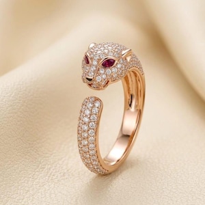 Op de afbeelding: Een roségouden ring in de vorm van een panter. De kop van de panter is bezet met kleine, heldere edelstenen en twee rode edelstenen als ogen. Het lichaam van de ring is ook bedekt met kleine, heldere edelstenen.