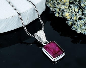 May include: A silver pendant necklace featuring a rectangular, deep red gemstone. The gemstone is set in a silver bezel and hangs from a delicate silver chain. The pendant's bail has an ornate, decorative design.