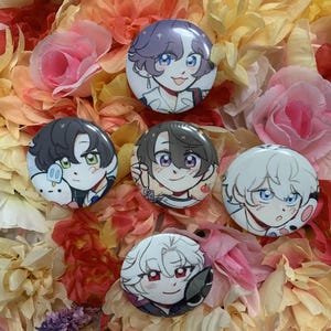 Puede incluir: Una colección de seis botones redondos de personajes de estilo anime con ilustraciones coloridas. Los botones presentan varios personajes con diferentes colores de cabello y expresiones. Los botones están dispuestos sobre un lecho de flores artificiales coloridas.
