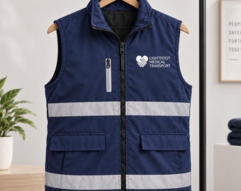 Pode incluir: Um colete azul-marinho sem mangas com fecho frontal, um pequeno bolso no peito com fecho e dois bolsos inferiores com aba. A peça inclui faixas refletoras prateadas horizontais e o logótipo branco Lightfoot Medical Transport.
